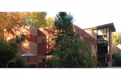 Brick multi-story building with trees in front and a glass entryway under a clear sky.