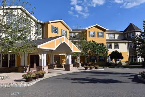 Exterior view of a multi-story assisted living building with a covered entrance and yellow facade.