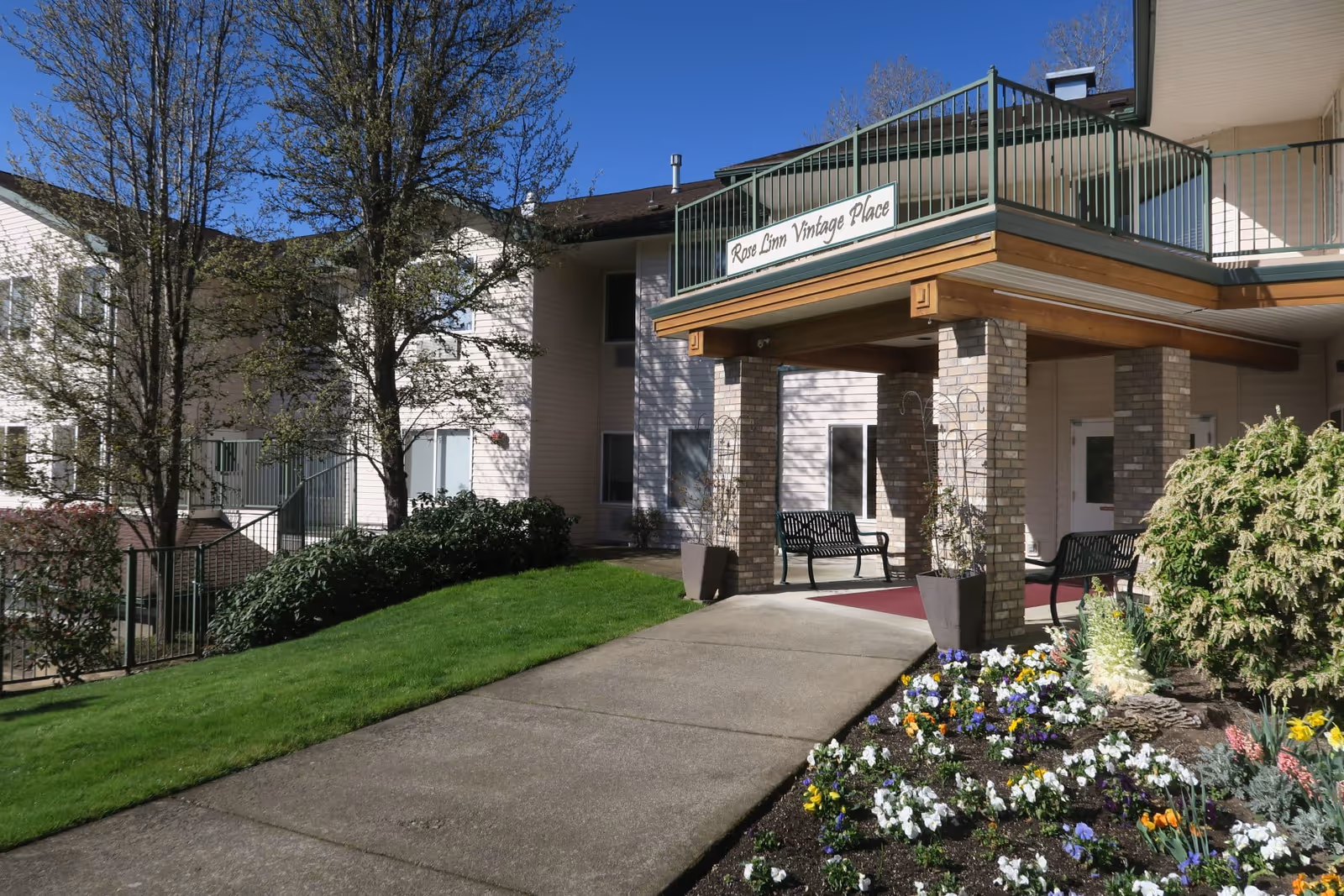 Front entrance of Rose Linn Vintage Place with a covered walkway, benches, and a flowerbed.