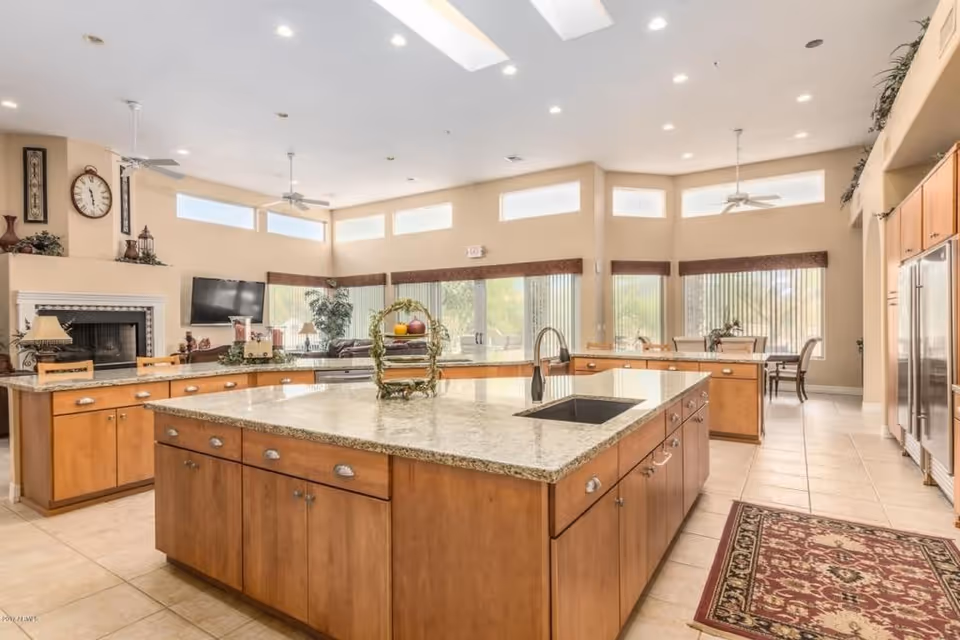 Spacious communal kitchen with multiple granite-topped islands, wooden cabinetry, a sink, and large windows.