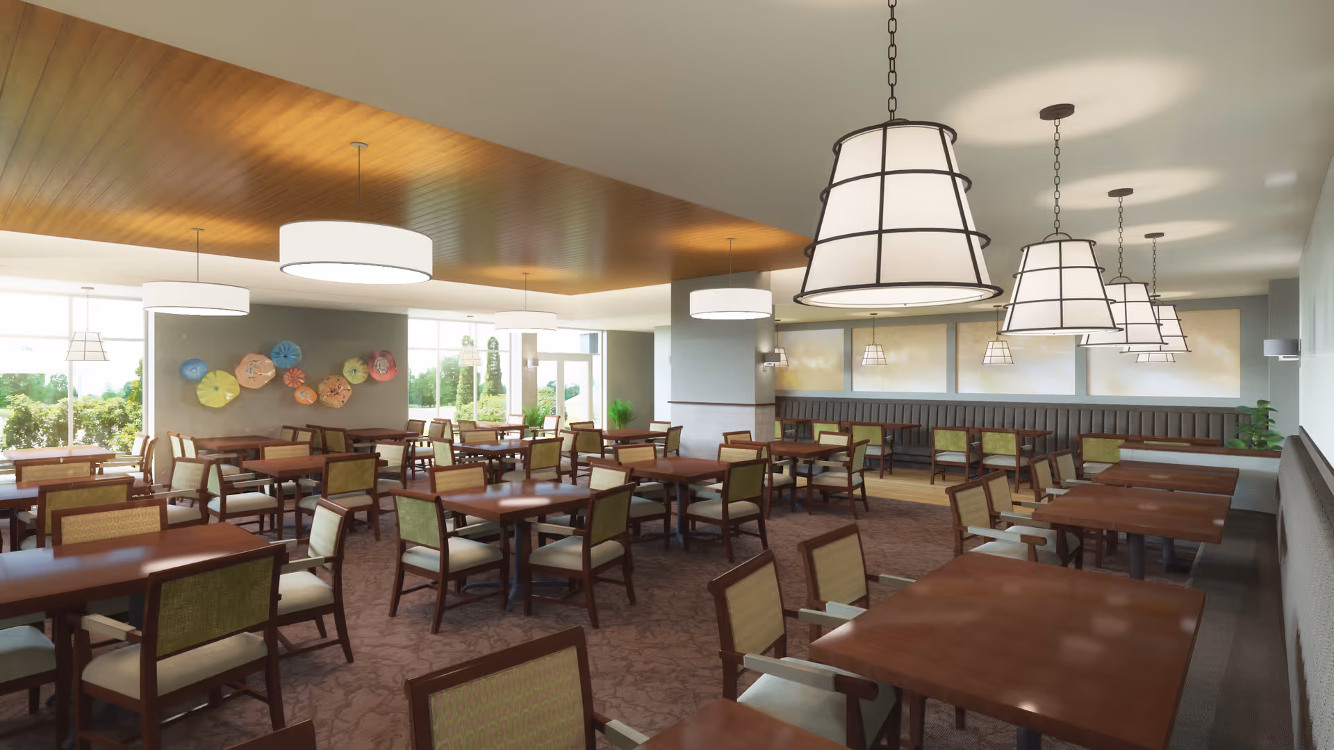 A spacious dining room with multiple wooden tables and chairs arranged neatly. The room features large hanging light fixtures, a wooden ceiling section, and large windows letting in natural light. Decorative wall art and plants add to the welcoming atmosphere.