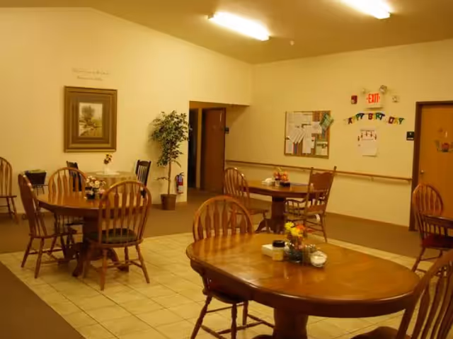 Community dining area with wooden tables and chairs, a bulletin board, and wall decorations.