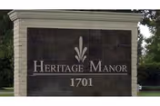 Stone monument sign with the text 'Heritage Manor 1701' displayed outdoors with trees and grass in the background.