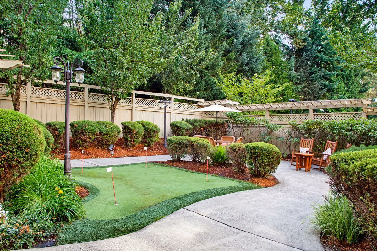 Well-maintained outdoor courtyard with a small putting green, seating area, pergola and landscaped shrubs.