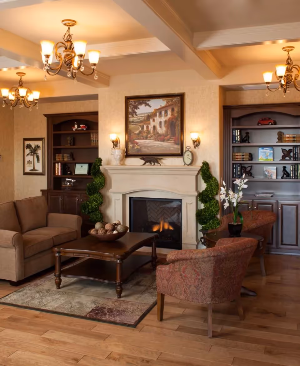 Comfortable living room with a lit fireplace, sofa and armchairs arranged around a wooden coffee table, built-in bookshelves, and decorative lighting.