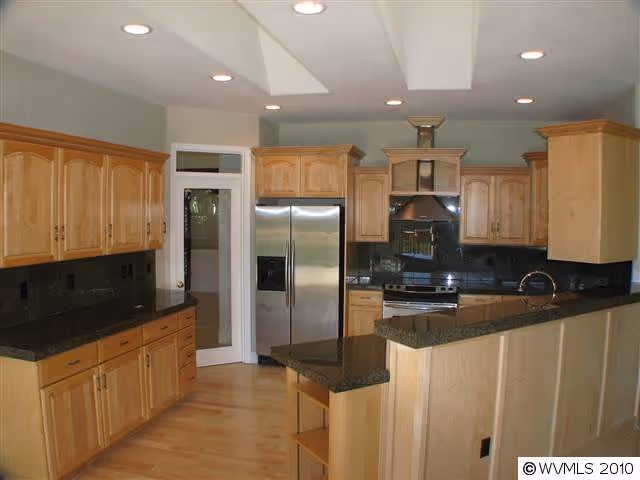 Spacious kitchen with light wood cabinets, black granite countertops, stainless steel appliances and a breakfast bar.
