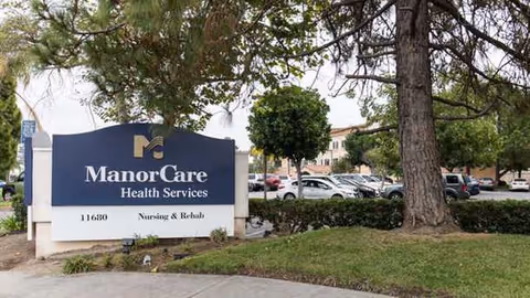 Exterior view of ManorCare Health Services sign with trees and a parking lot