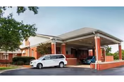 Front view of a brick senior living facility with a covered entrance and parked cars.