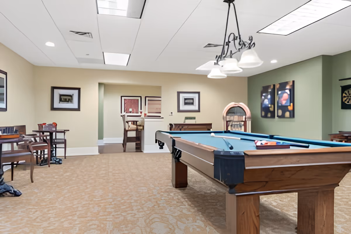 A spacious indoor recreation room featuring a pool table, seating areas, framed artwork, and a jukebox.