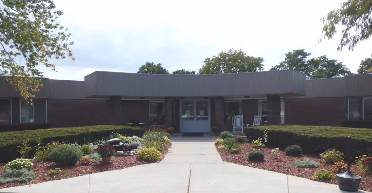 Front exterior view of Clearstream Rehabilitation and Nursing Center showing a single-story building with a flat roof, a central entrance with double glass doors, surrounded by landscaped bushes, plants, and a small garden area with a water feature.