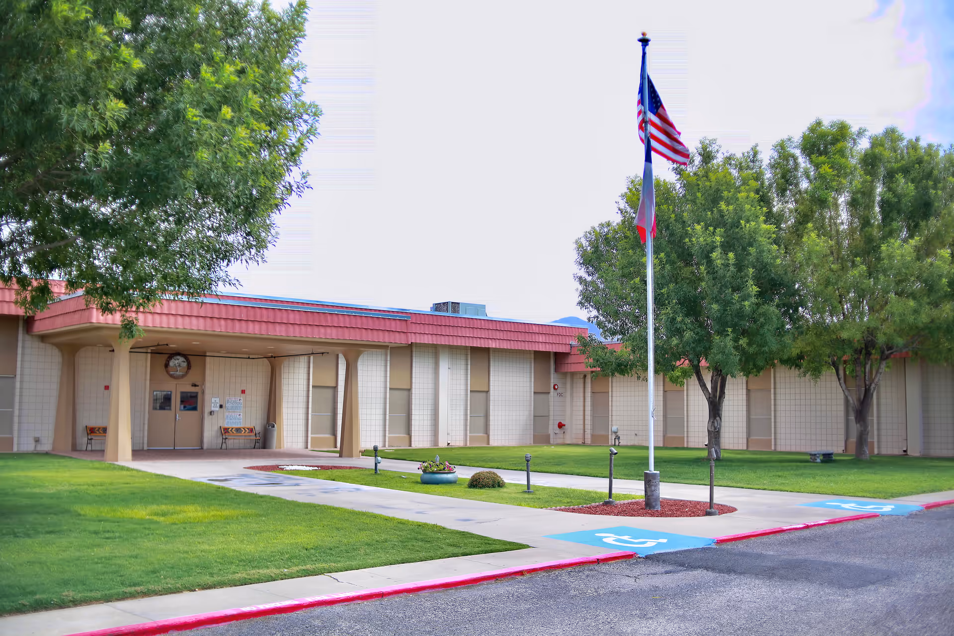 Entrance of a single-story nursing facility with a flagpole flying an American flag, a manicured lawn and trees.