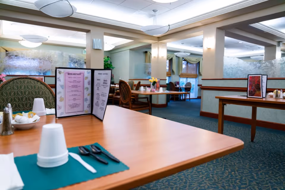 Spacious dining room with set tables, menus, and chairs in a senior living facility.
