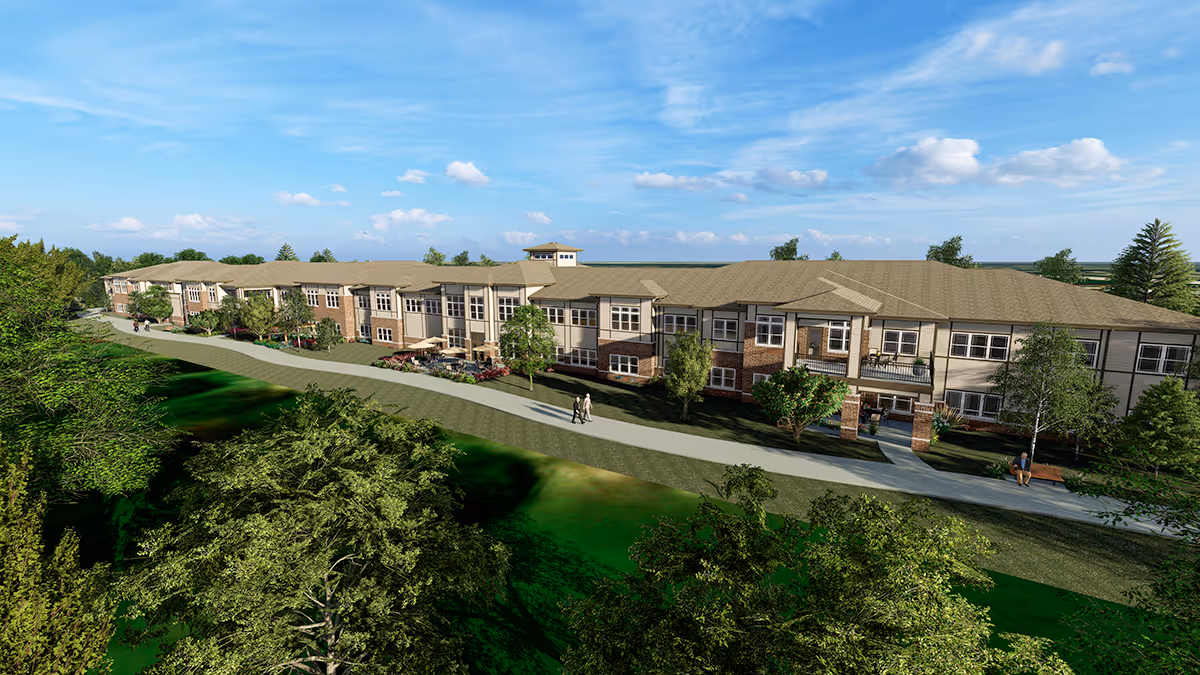 Exterior view of a long two-story senior living building surrounded by trees, lawn, and a walking path under a blue sky.