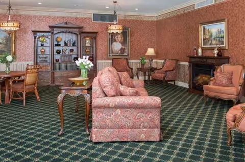 Traditional hotel-style living room with red patterned wallpaper, green carpet, and upholstered seating.