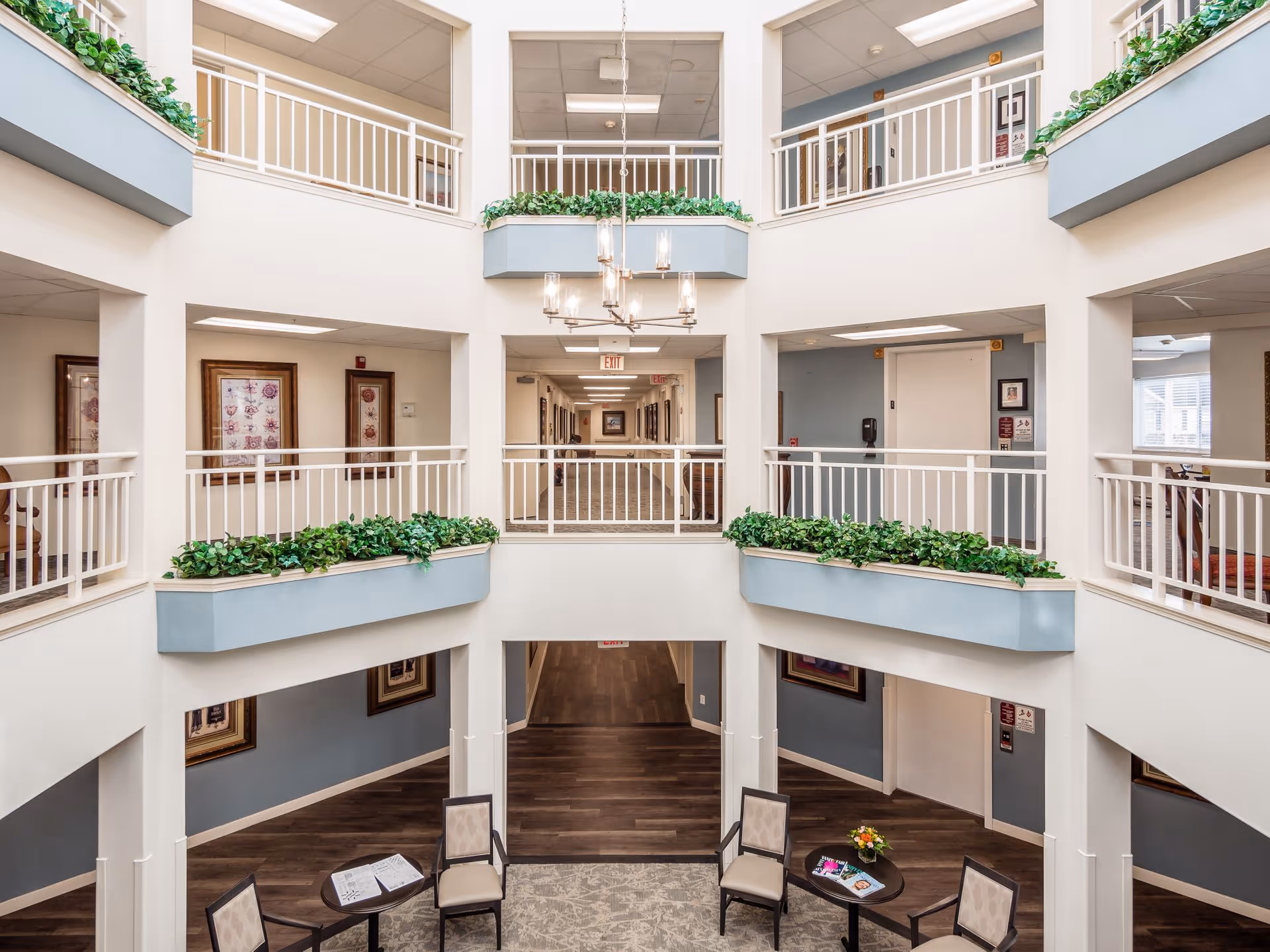 Bright multi-level interior atrium with balconies, planted ledges, a central chandelier and a small seating area.