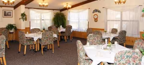 Dining room with round tables, floral upholstered chairs, and white table linens.