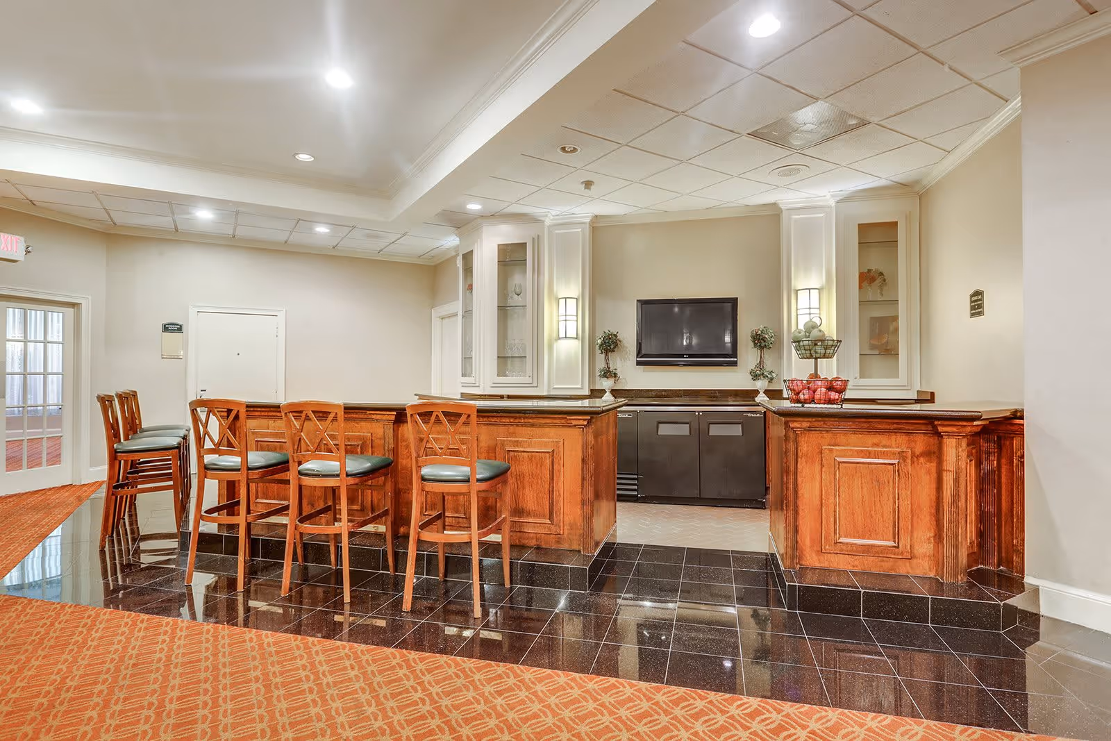 Interior common-area bar with wooden counters, five barstools, and a wall-mounted TV.