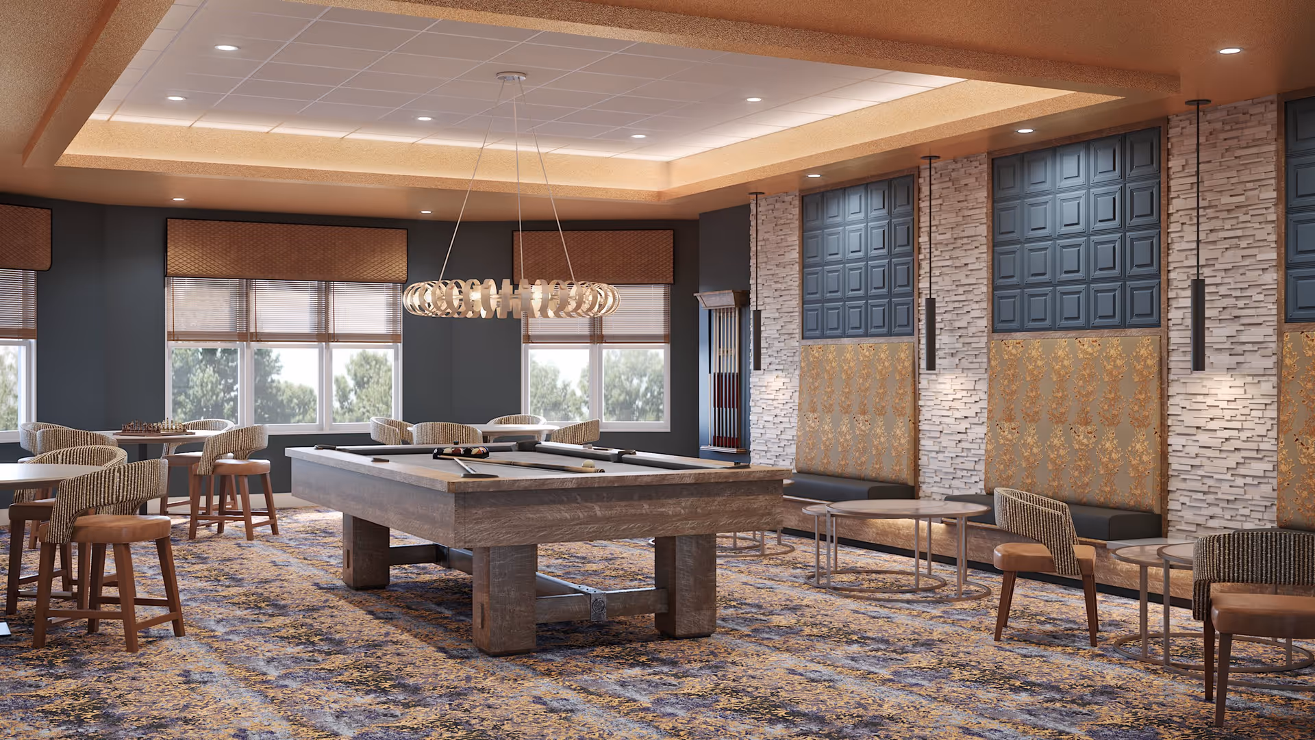 A spacious recreational room with a pool table in the center, surrounded by chairs and small tables. The room features large windows with blinds, a modern circular chandelier hanging above the pool table, and decorative wall panels with textured and patterned designs. The carpet has a multicolored pattern, and there is a rack with pool cues on the wall.