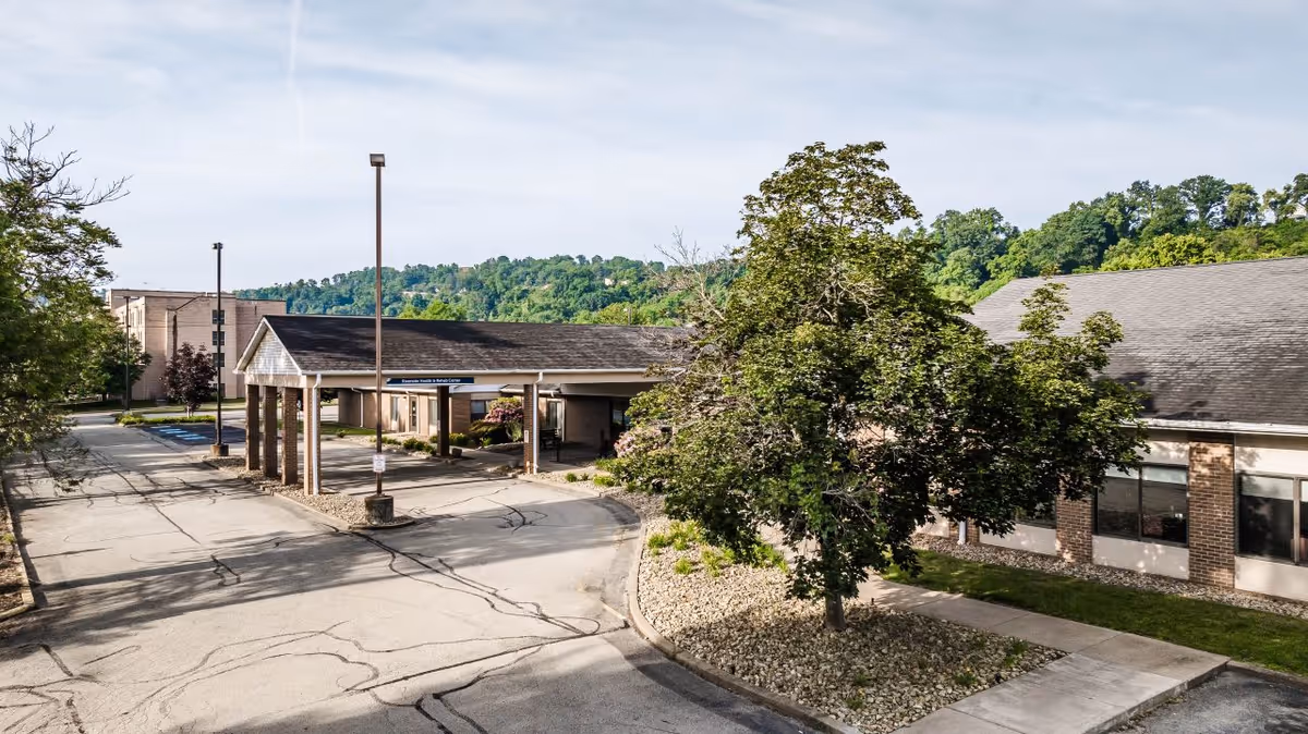 Covered driveway and main entrance of a health and rehab center with trees, walkways, and a paved parking area.