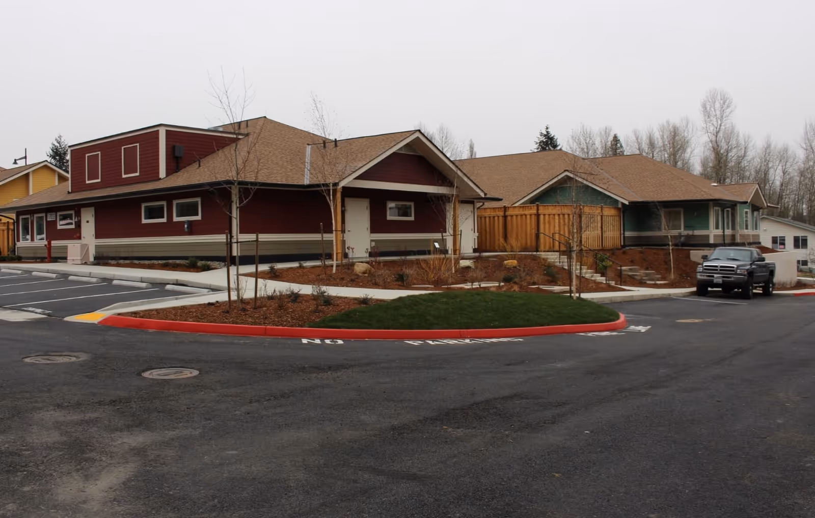 Single-story cottage-style senior living buildings with a parking lot and landscaped island under an overcast sky.