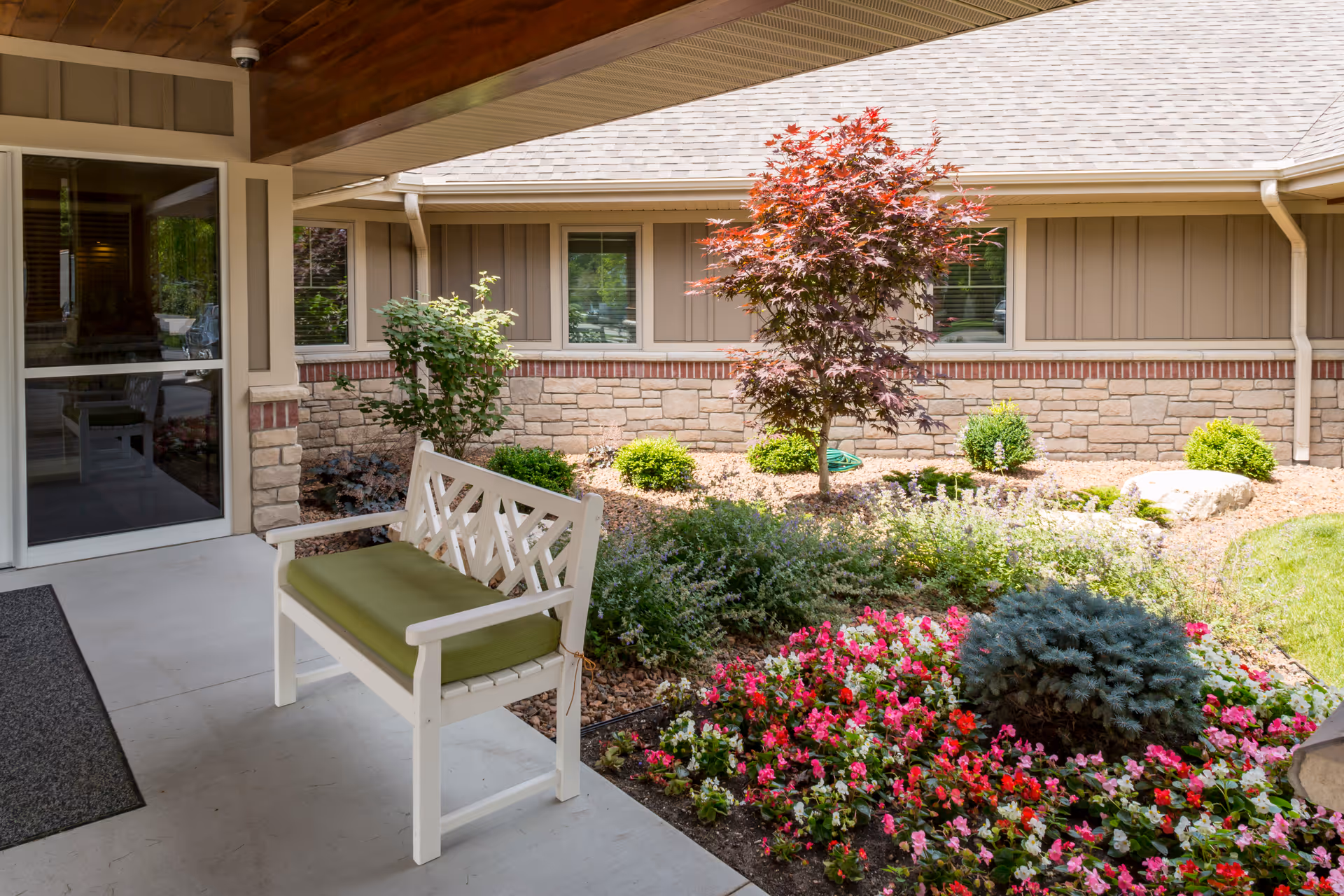 Covered entry courtyard with a white bench, landscaped flower beds, and a small tree in front of the building.