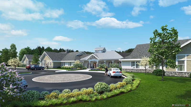 Single-story senior living building with a circular drive, parked cars, and landscaped lawns under a blue sky.