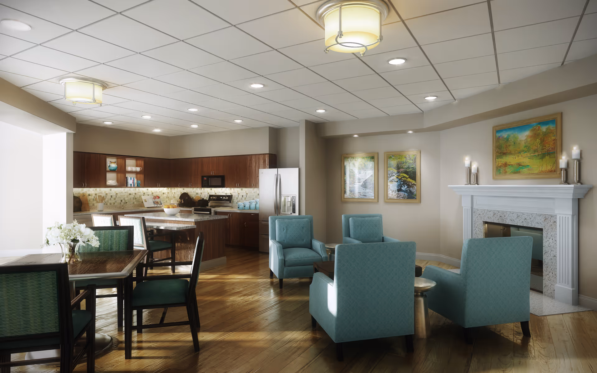 A bright and spacious senior living common area featuring a kitchen with dark wood cabinets, stainless steel refrigerator, stove, and microwave. The room includes a dining table with green cushioned chairs, a seating area with four light blue armchairs around a coffee table, and a white fireplace adorned with candles and a landscape painting. The walls have additional framed nature artwork, and the floor is polished wood.