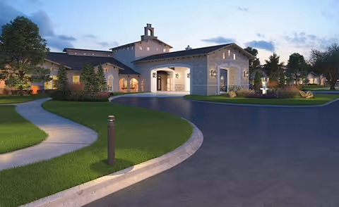 Exterior view of a senior living facility building at dusk with well-maintained landscaping, a curved driveway, and illuminated entrance.