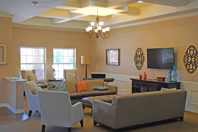 Communal living room with sofas, armchairs, a coffee table, wall-mounted TV, and a chandelier.