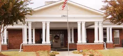 Brick senior living facility with a columned porch and an American flag at the entrance.