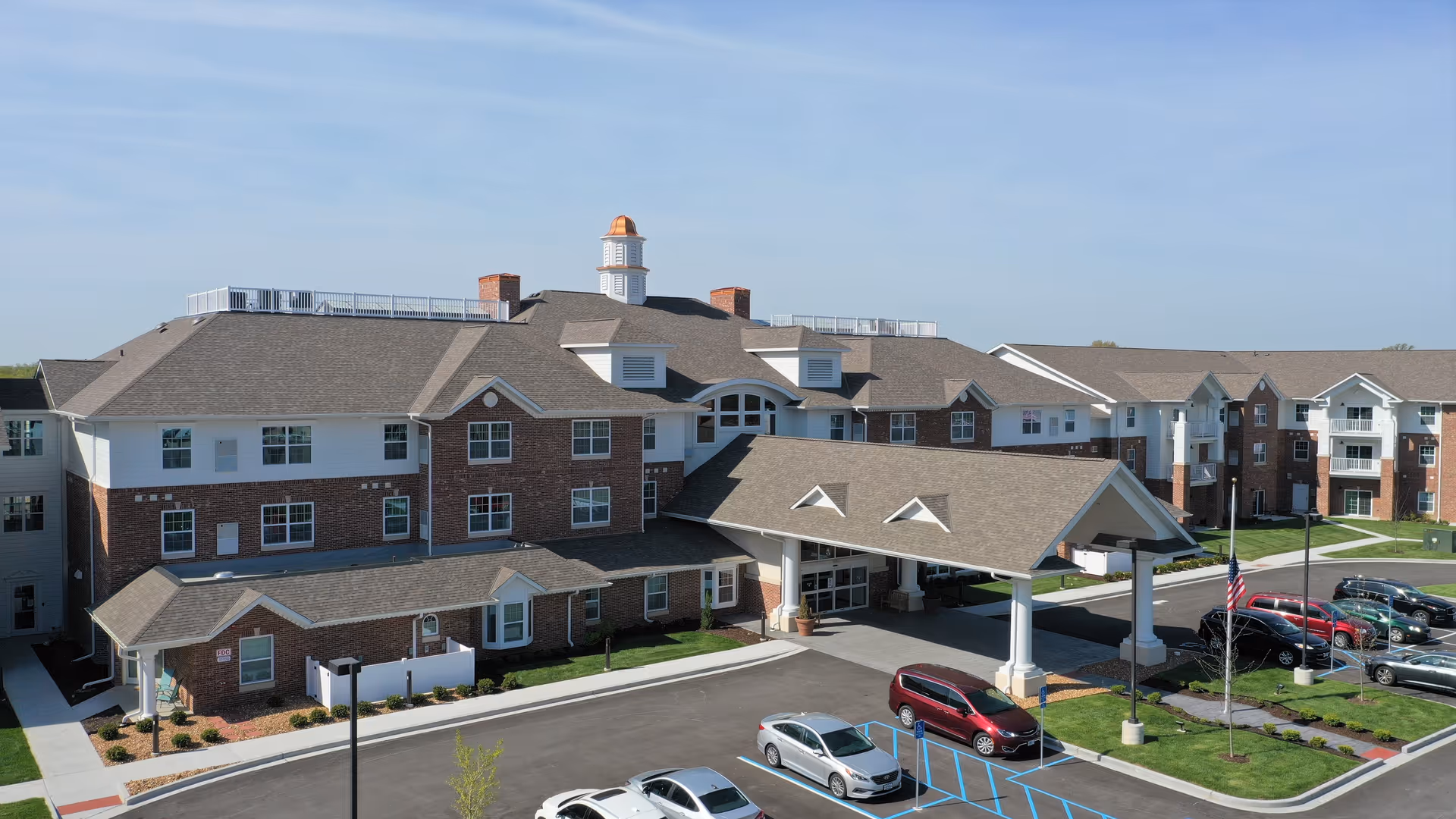Front exterior of a multi-story brick senior living building with a covered entry porte-cochère and parking lot.
