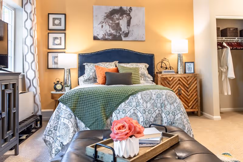 Well-decorated bedroom with a patterned bed, green throw, bedside tables with lamps, and an open closet.
