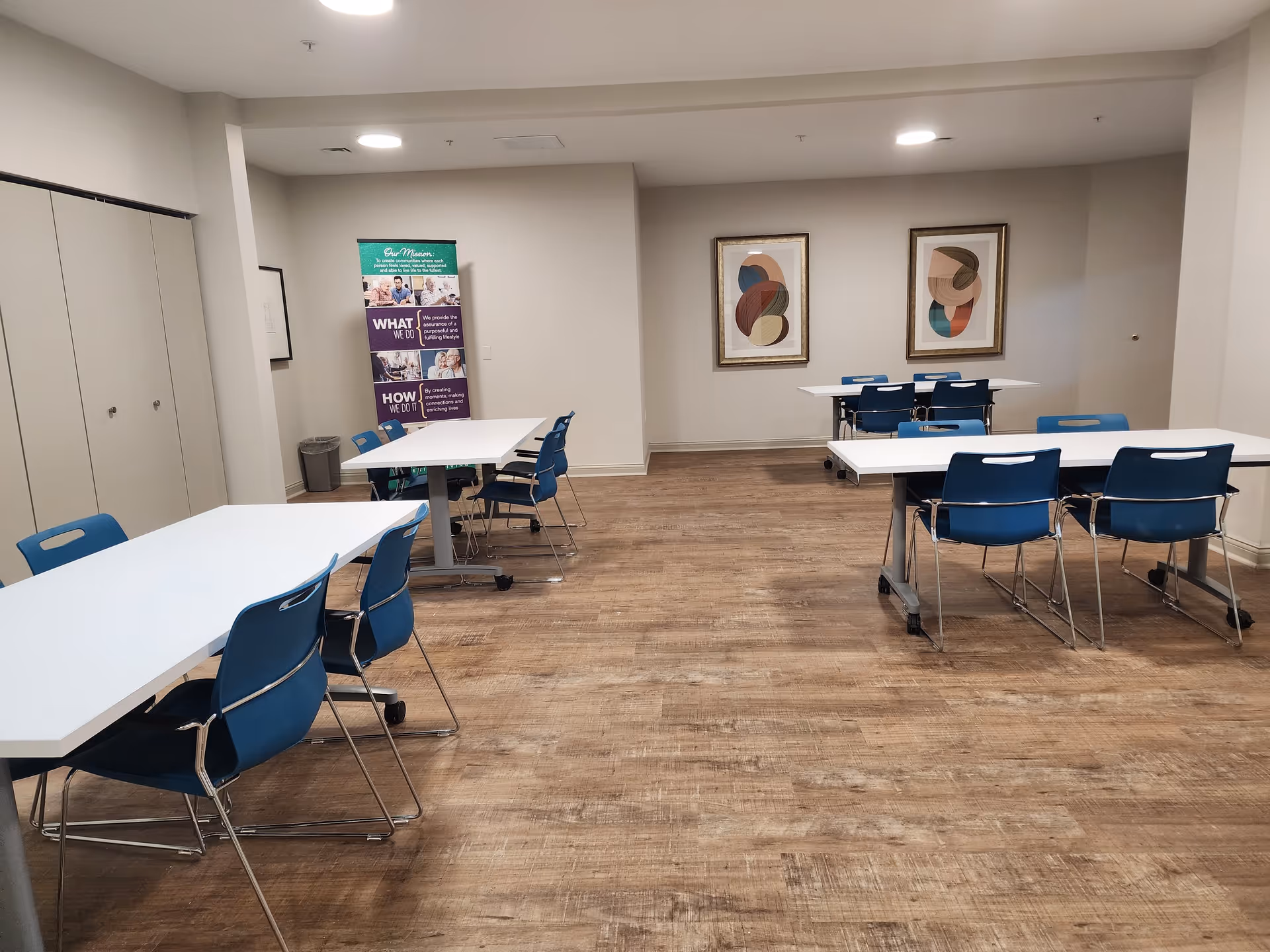 Interior view of a dining room with white tables and blue chairs, featuring framed artwork on the walls and a banner in the corner.