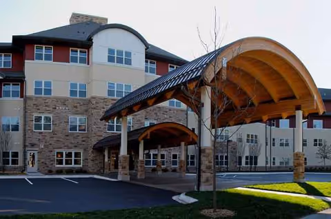 The Glenn Minnetonka senior living facility exterior with curved wooden entrance canopy and parking lot.