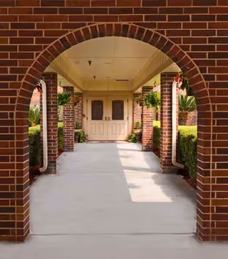 Brick archway corridor with hanging plants framing a double-door entrance.