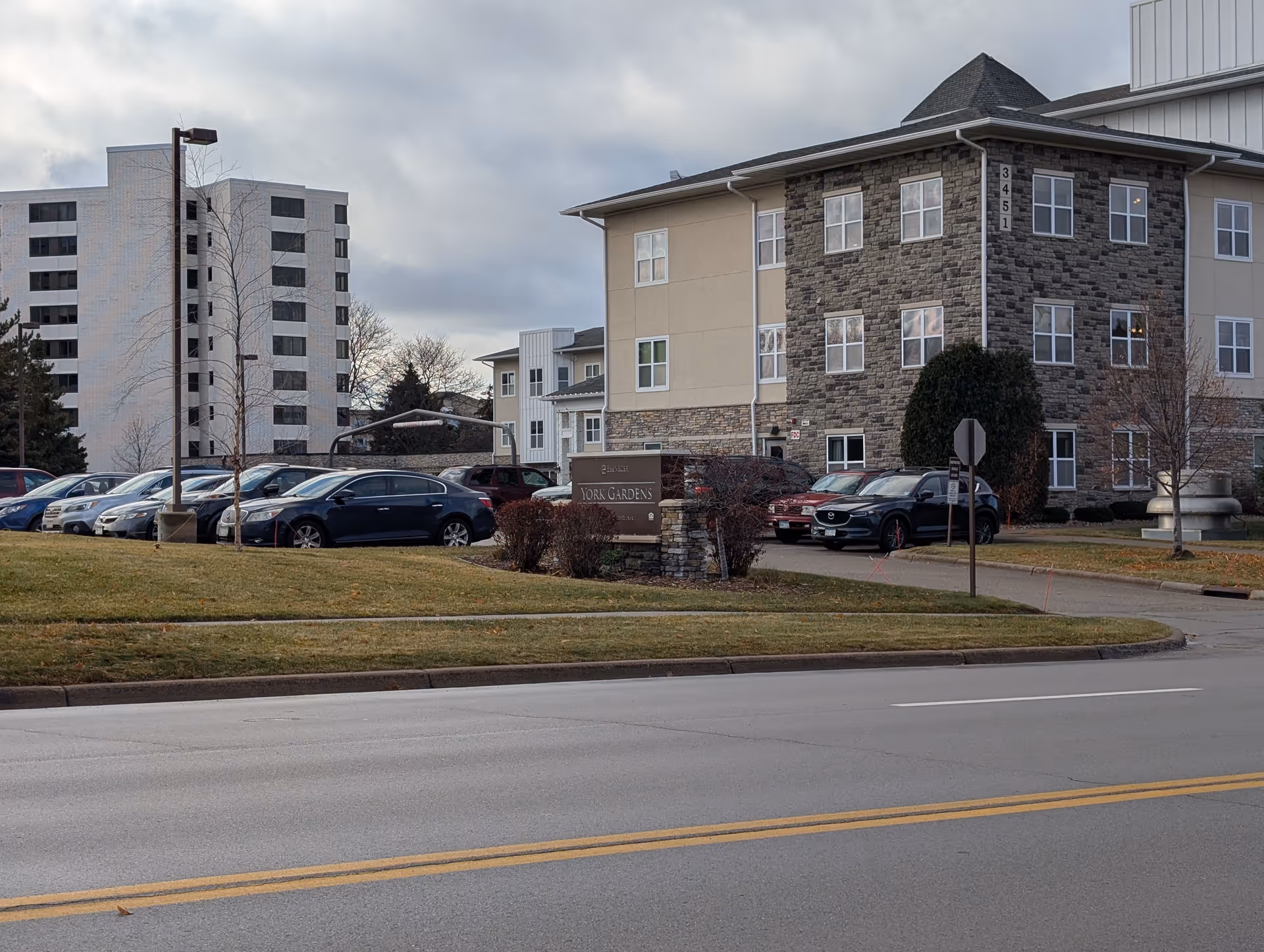 Exterior front of the York Gardens senior living building with a lawn, sign, and parked cars.
