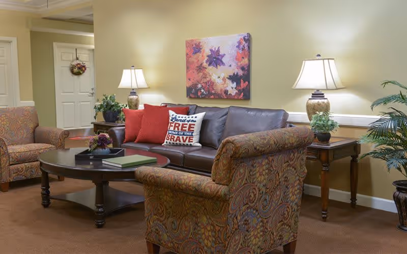 A cozy living room seating area with a leather sofa, patterned armchairs, a coffee table, table lamps and colorful wall art.
