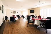 Spacious dining room with round tables draped in tablecloths, chairs, a fireplace with a wall-mounted TV, and large windows letting in daylight.