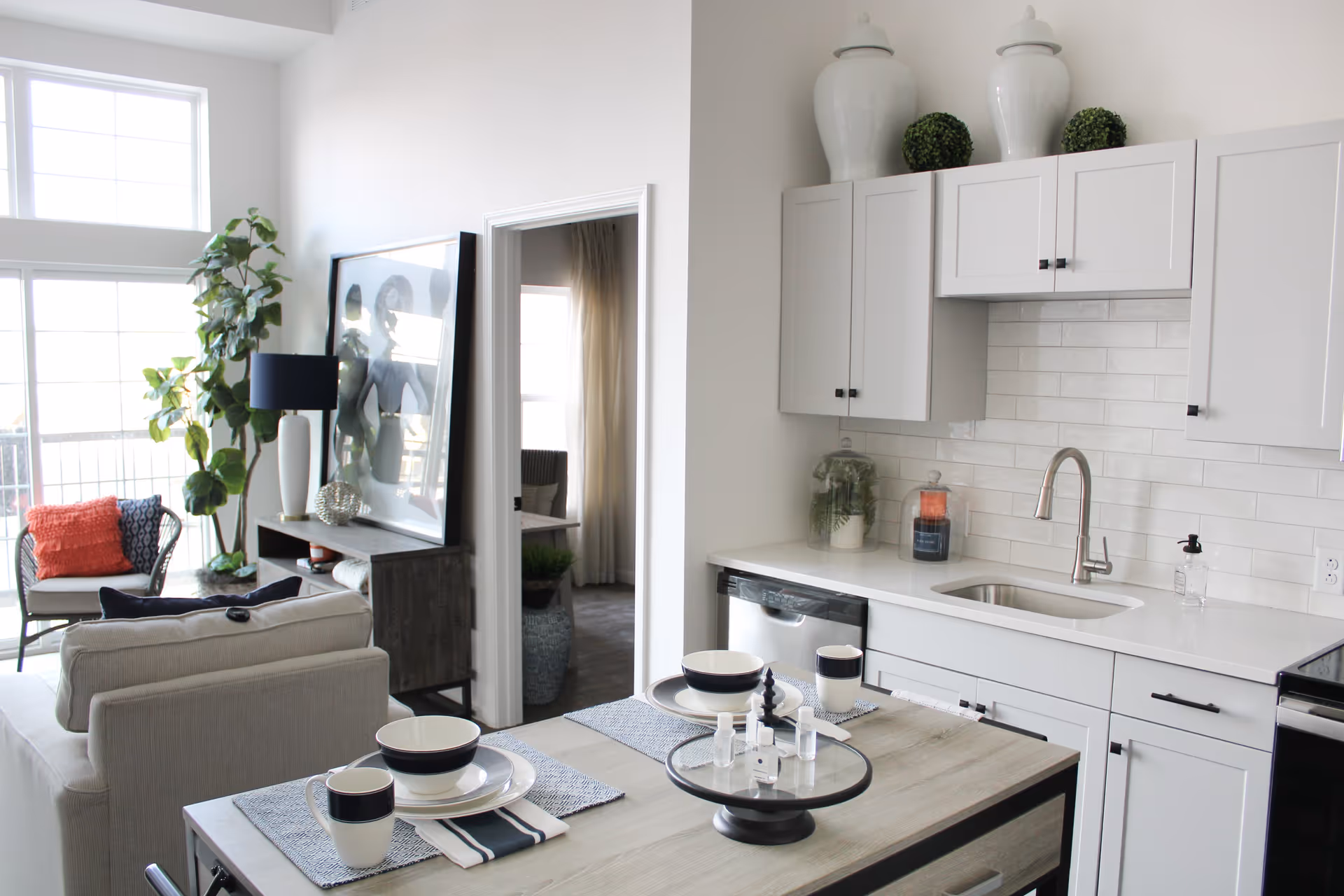 Open-plan kitchen and living area with white cabinets, a sink, a set dining table, and seating by tall windows.