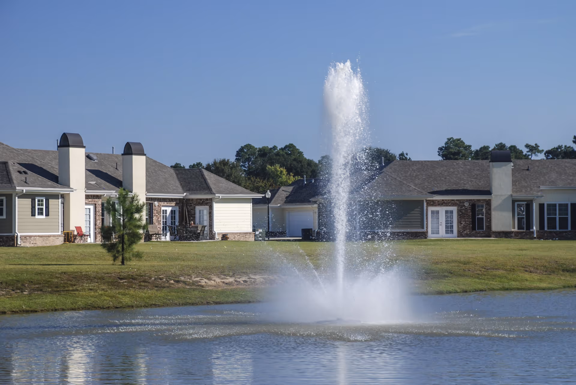 Exterior view of The Verandah Retirement Community with a central fountain and green lawn