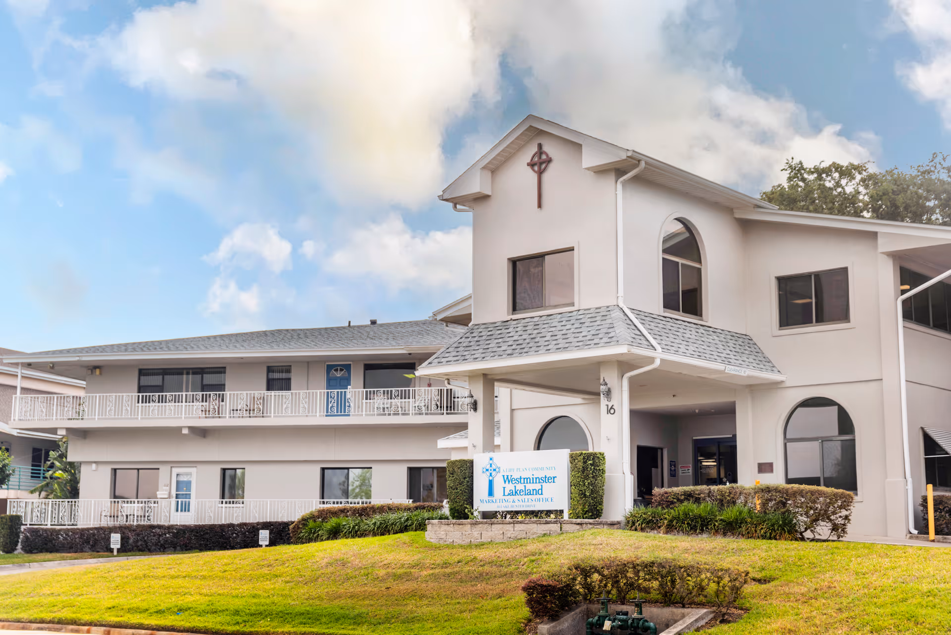 Front exterior of the Westminster Lakeland senior living building with a covered entrance and sign on a grassy lawn.