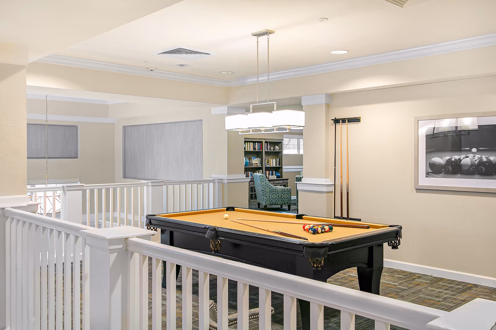 Bright interior common room featuring a pool table, cues, seating and bookshelves.