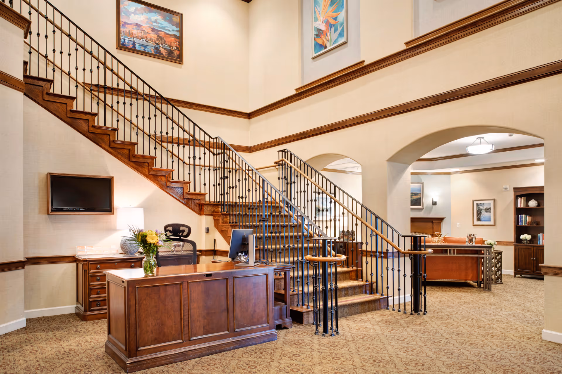 Elegant interior lobby with a wooden reception desk and a sweeping staircase with wrought-iron railing.