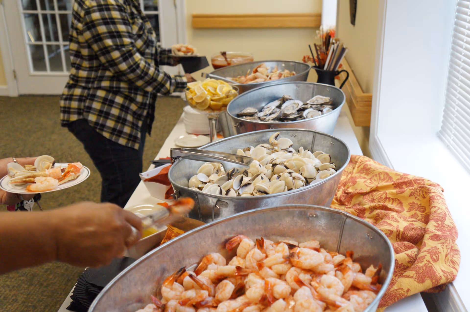 Metal tubs of shrimp, clams and other seafood on a buffet table as guests serve themselves.
