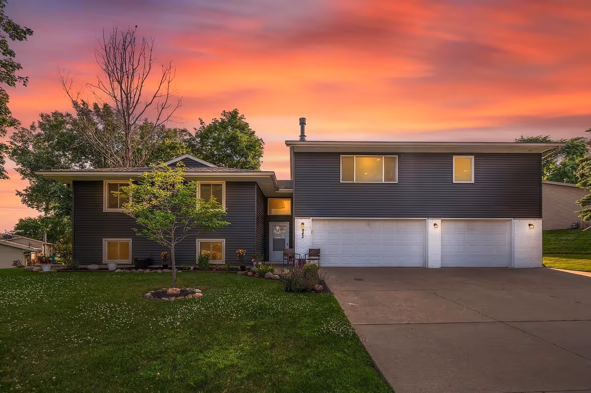 Two-story modern house with dark siding, attached three-car garage, and a well-kept lawn at dusk.