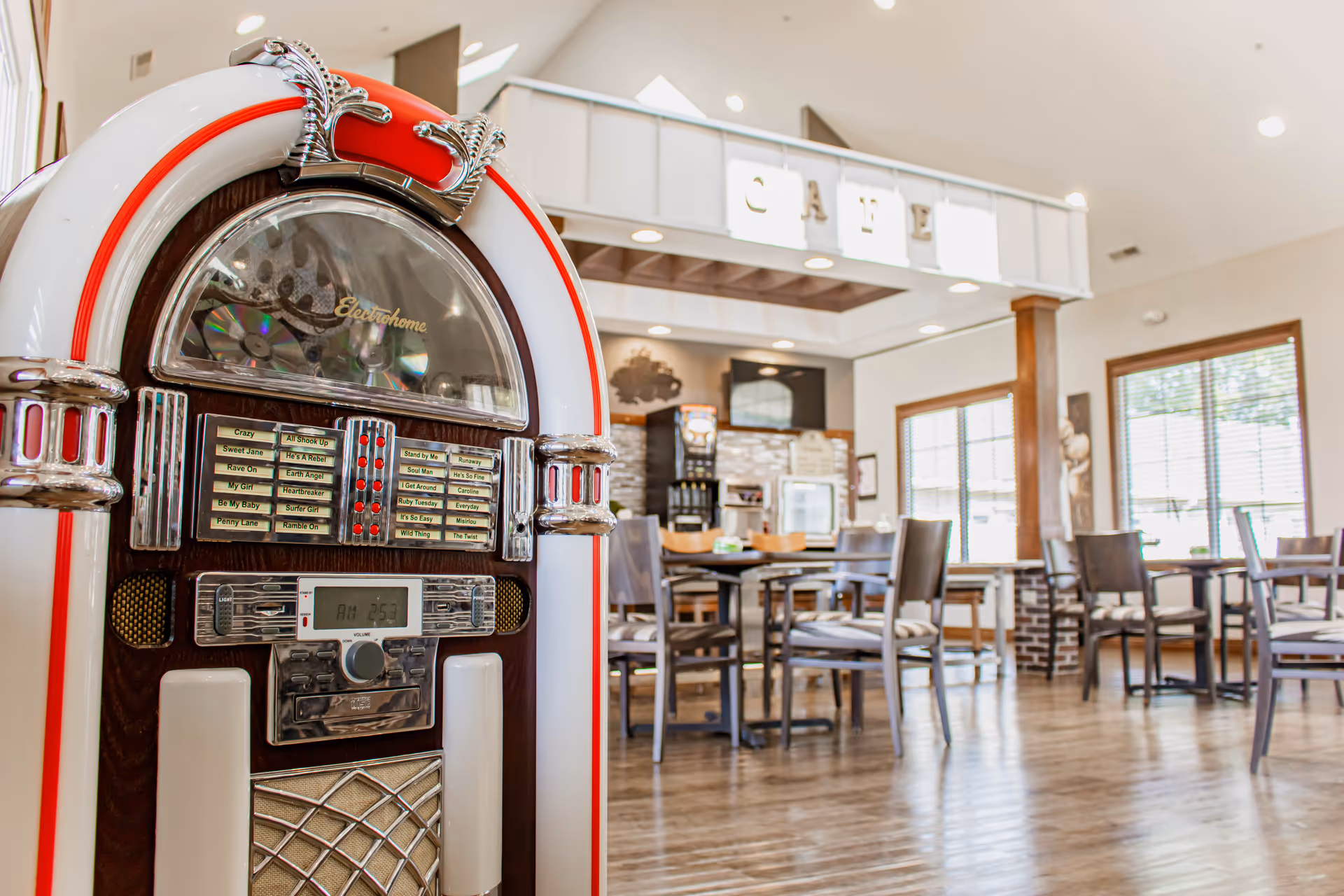 A vintage jukebox in the foreground of a bright dining café with tables and chairs in an assisted living facility.