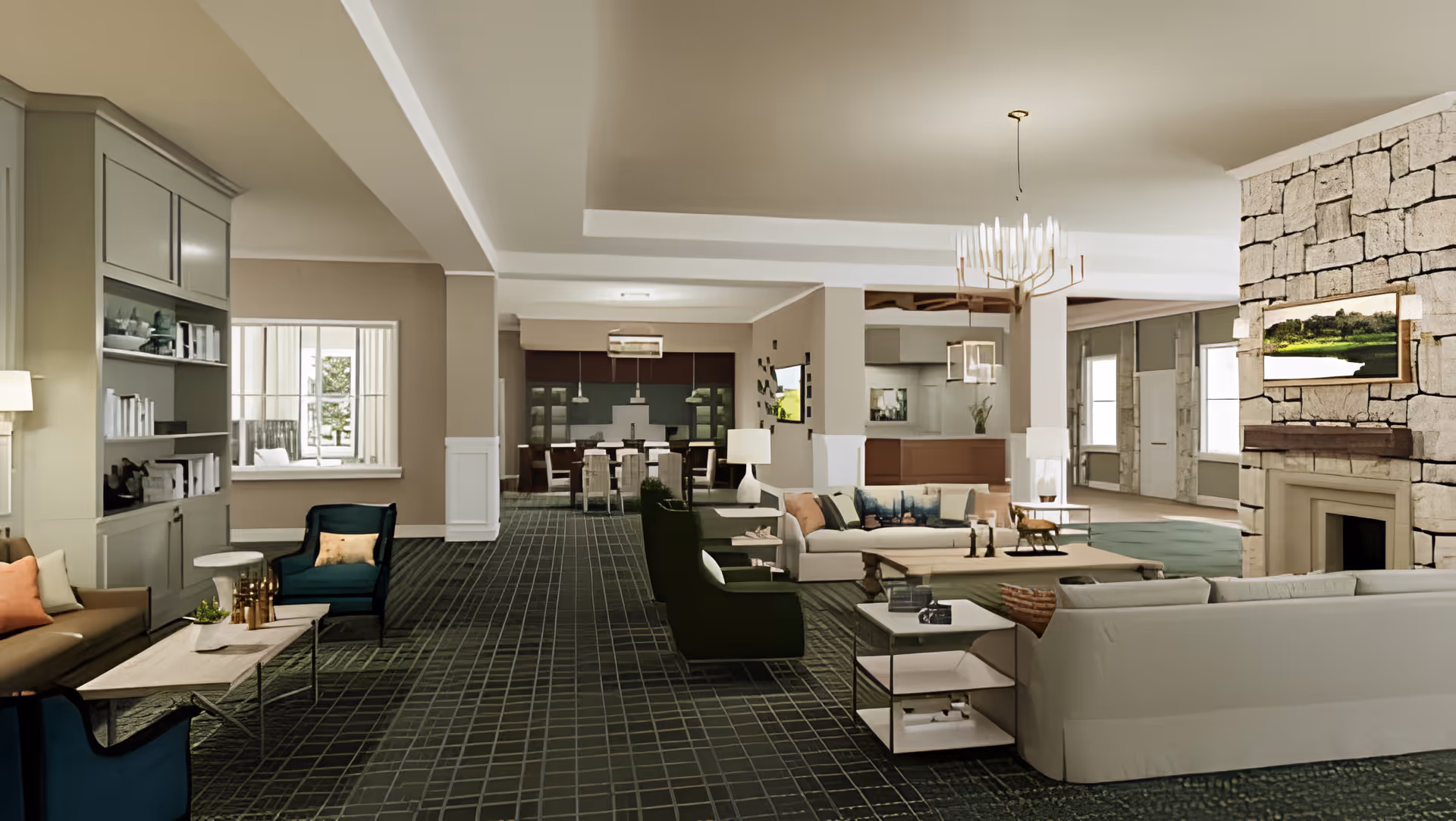 Spacious senior living facility common area with multiple seating arrangements including sofas and armchairs, a stone fireplace with a mounted landscape painting, carpeted floor with a grid pattern, and a dining area in the background under modern light fixtures.