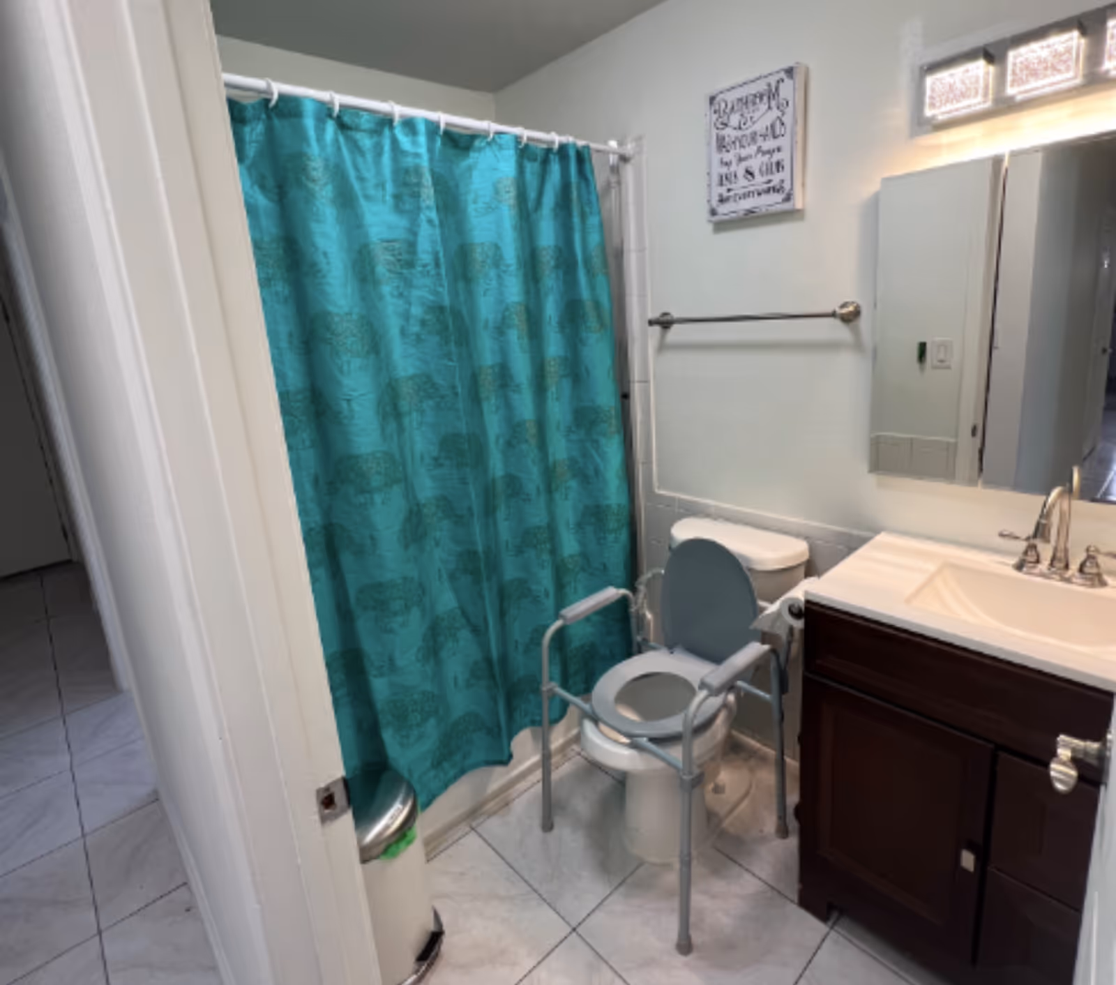 Small bathroom with teal shower curtain, toilet, walker, sink, and mirror.