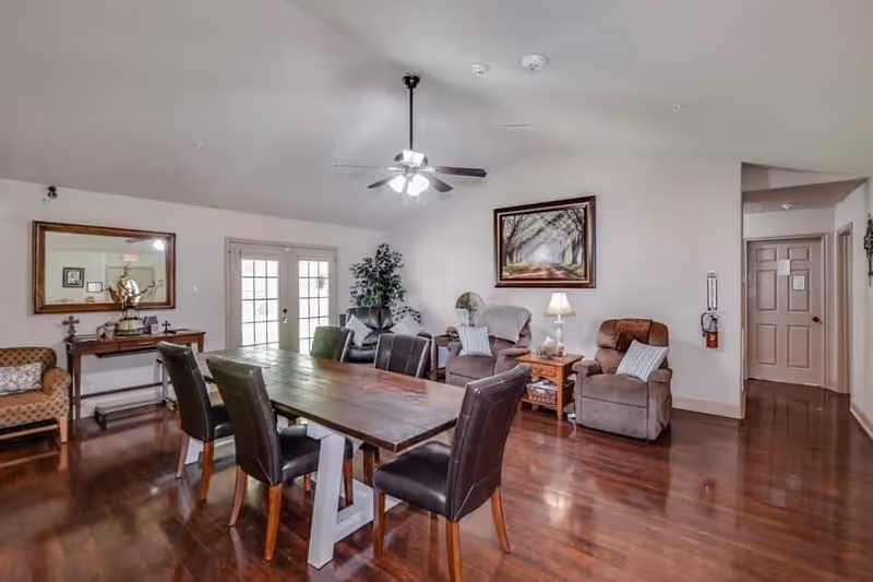 Communal dining and sitting area with a long wooden table, leather chairs, recliners and wall art.