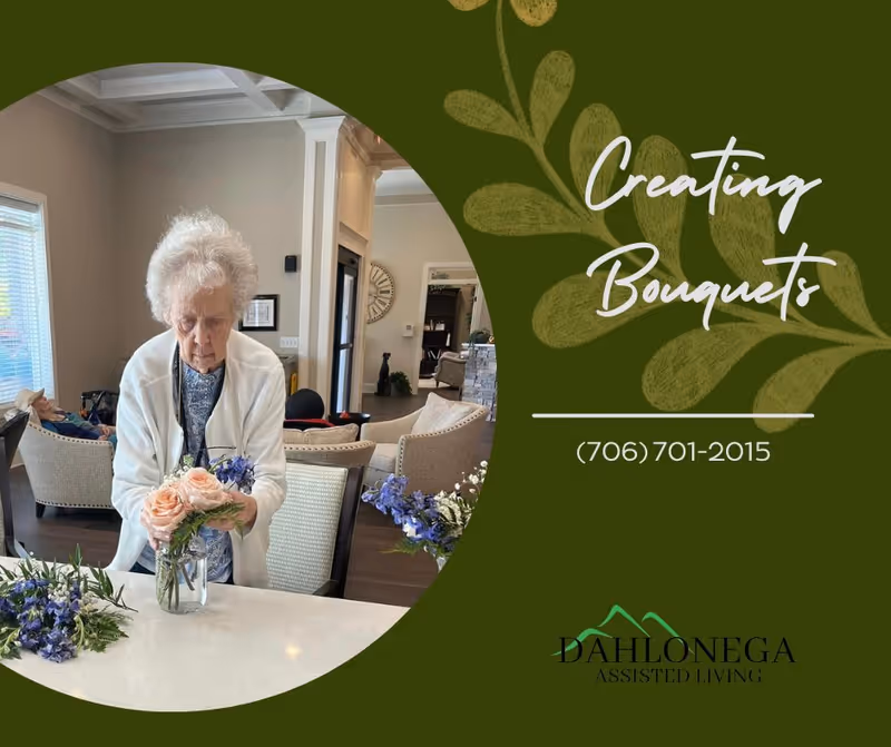 An elderly woman arranging a bouquet of flowers in a glass vase on a white countertop inside a living room area with chairs and a large clock on the wall.